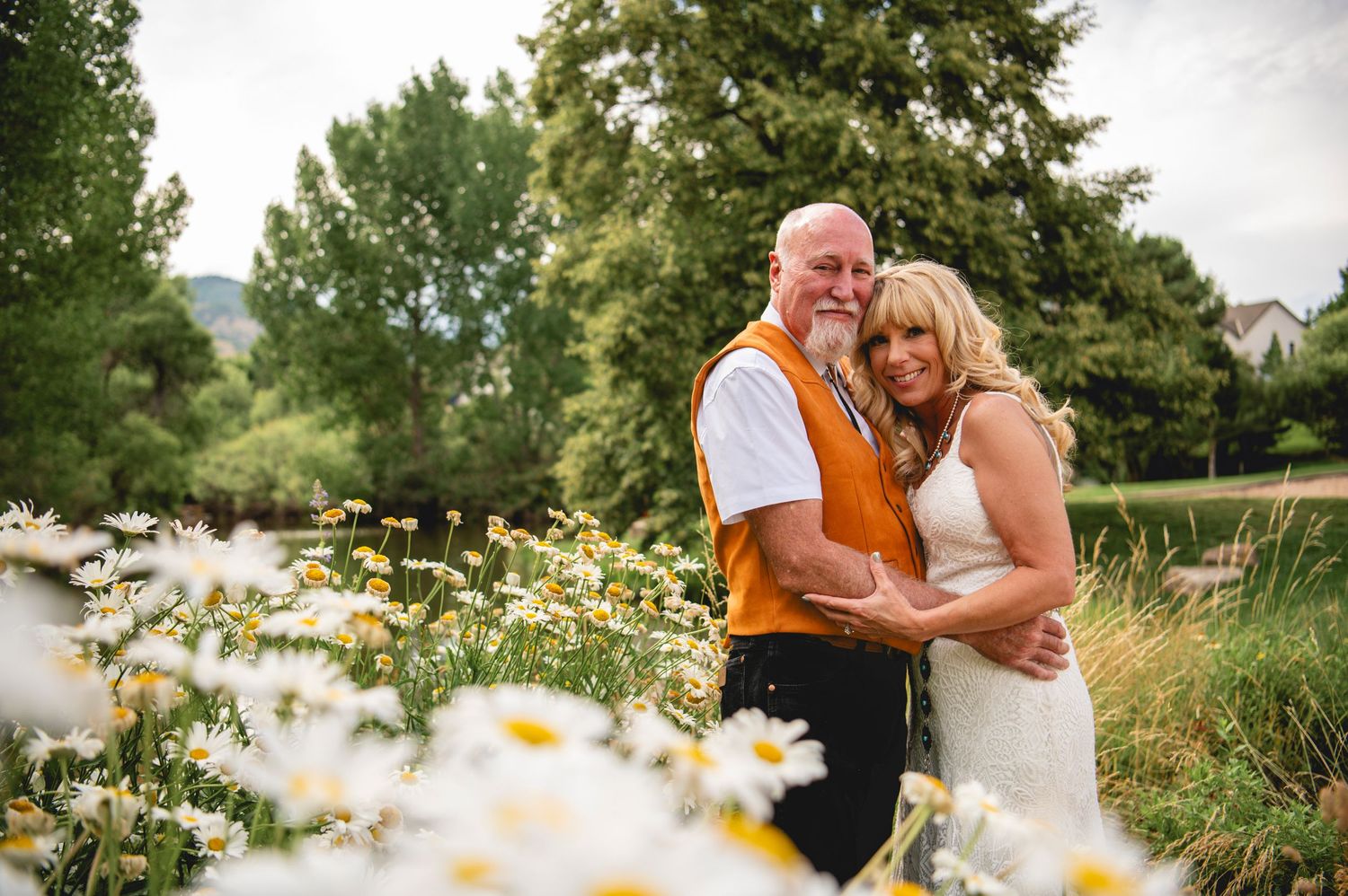 A loving embrace outdoors in a garden with white daisies blooming in the foreground during golden hour lighting.