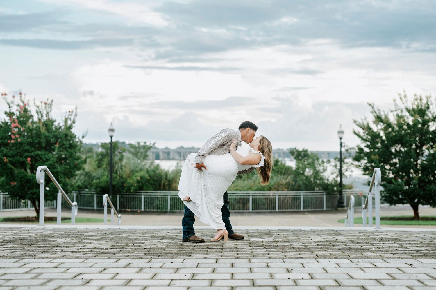 A couple poses creatively on a stone paved walkway with trees in background.