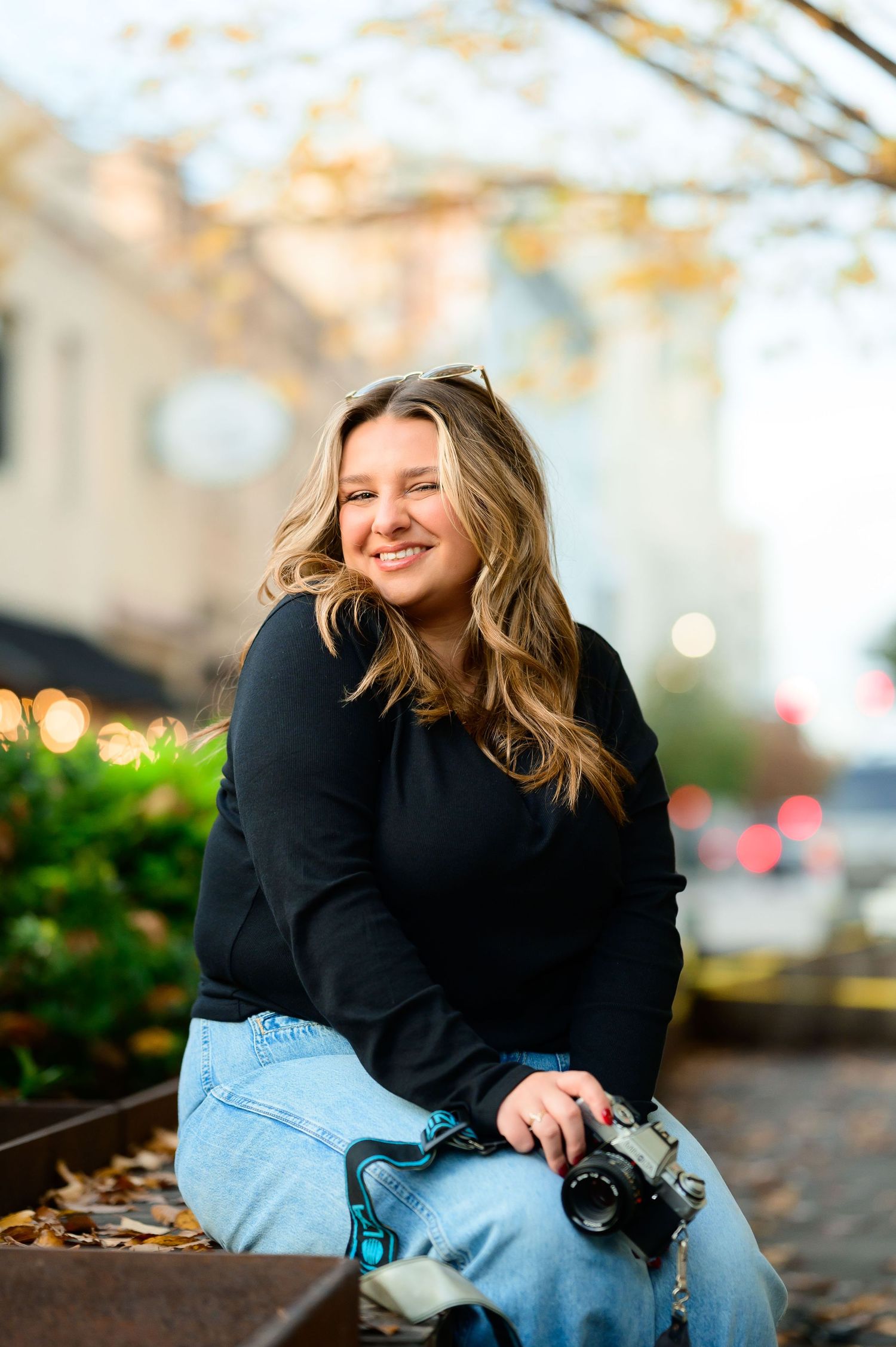 Person in dark sweater and jeans poses casually with camera during autumn photoshoot.