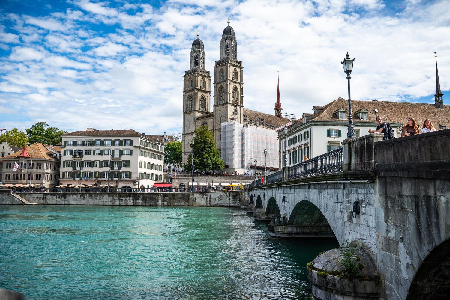 Panoramic view of Zurich cityscape with historic buildings and church spires along Lake Zurich under blue cloudy skies.