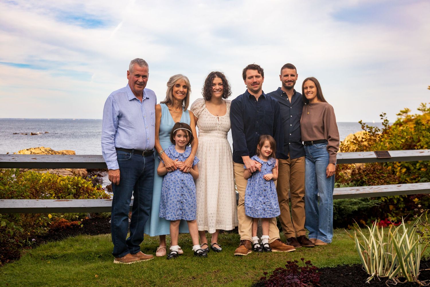 A group of people standing together outdoors at sunset with coastal scenery in the background.