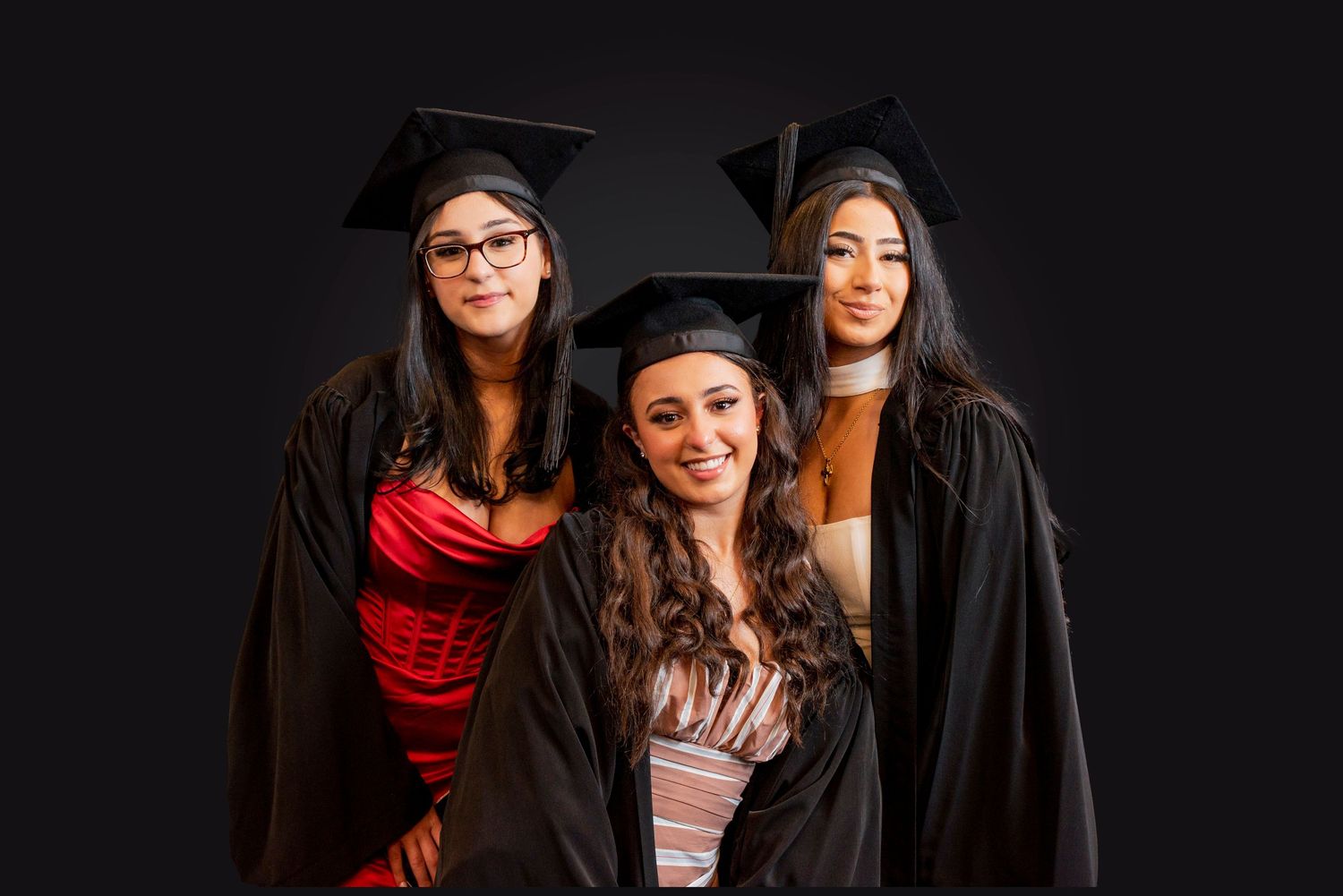 A group of friends wearing graduation caps and gowns pose together against a dark background.