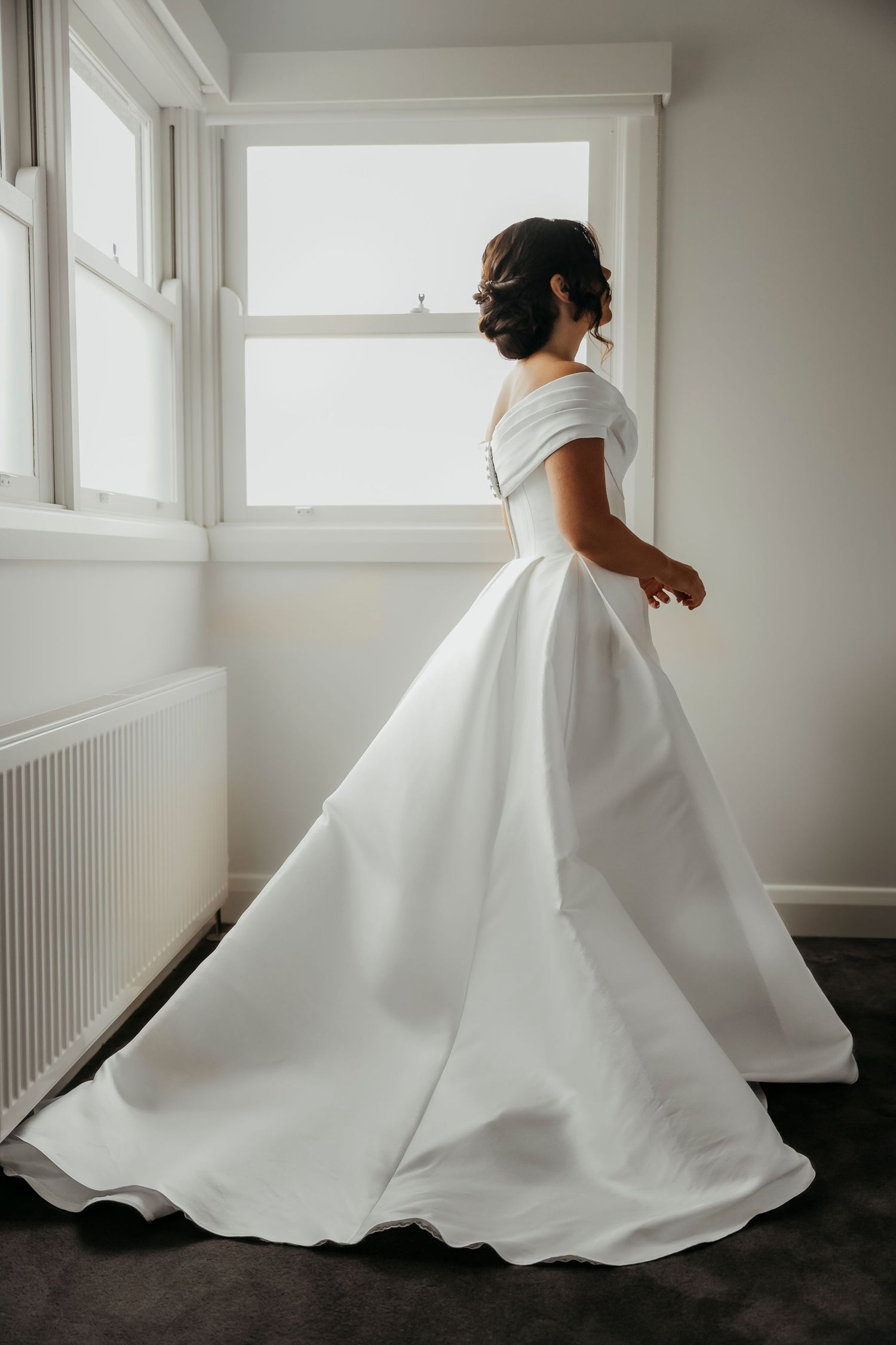 A flowing white wedding dress twirls elegantly in a bright minimalist room with dark flooring.