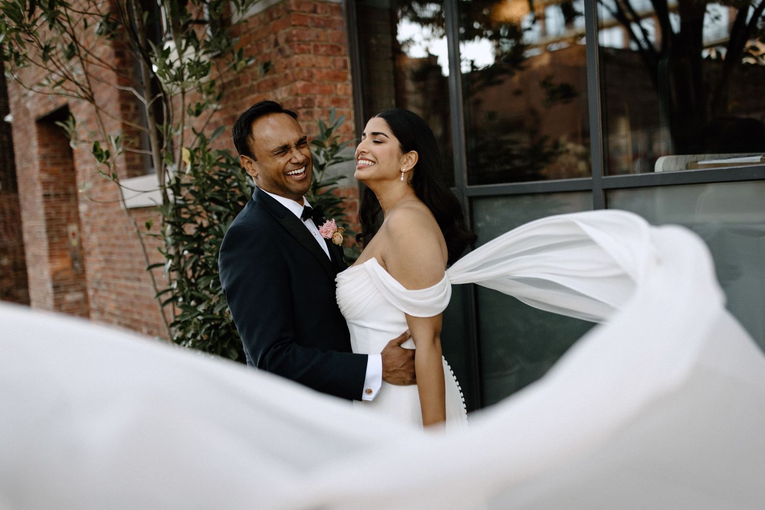 A romantic wedding moment outside a rustic brick building with string lights.