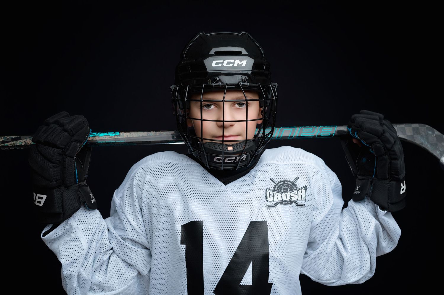Hockey player wearing white jersey and helmet stands ready in athletic stance on the ice.