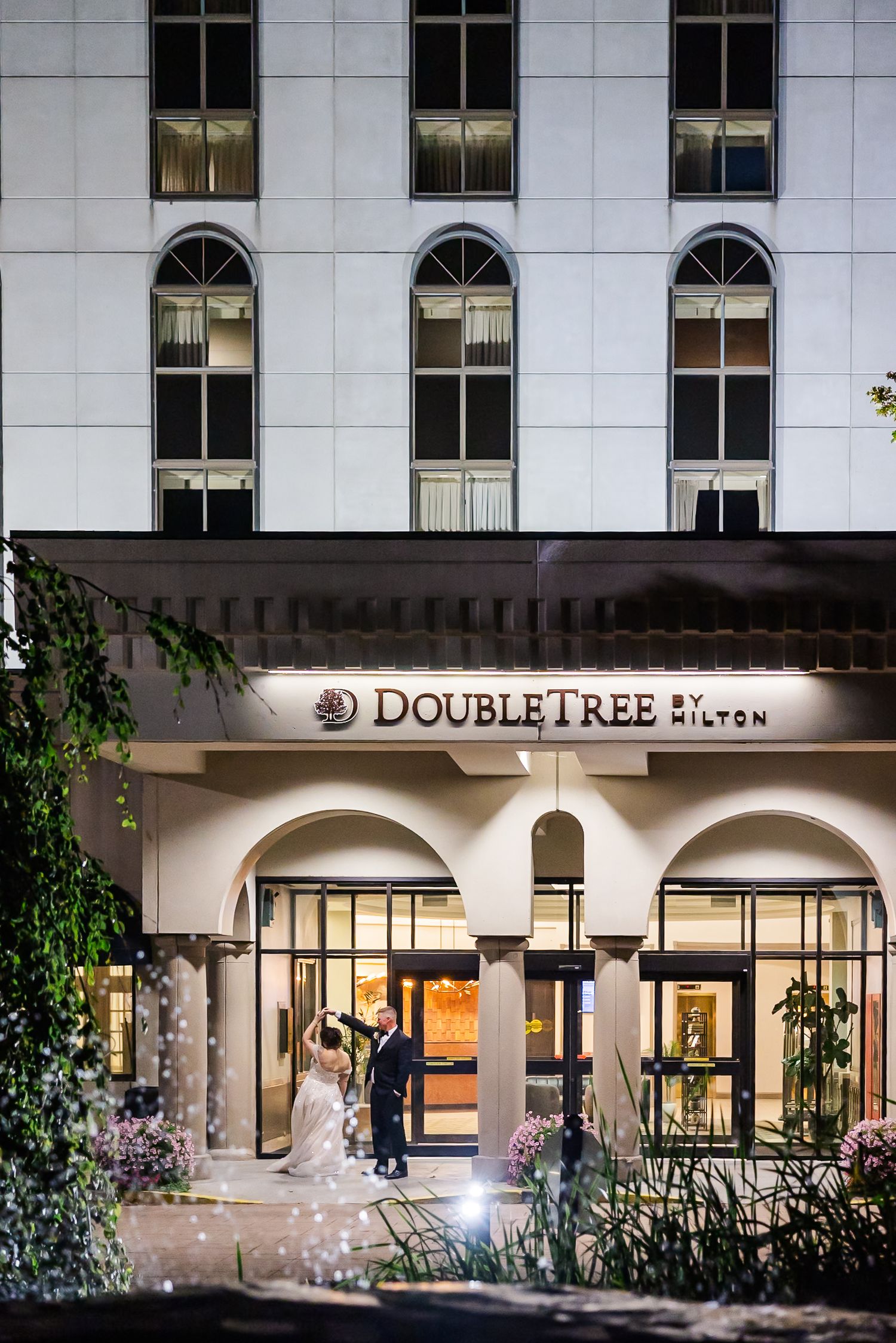 Illuminated entrance of DoubleTree Hotel at night with white columns and arched windows creating an elegant facade.