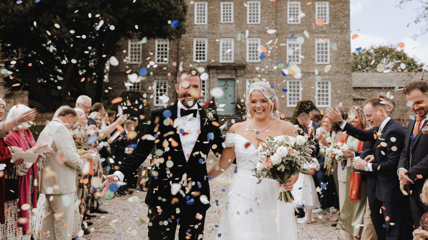 Wedding guests shower newlyweds with confetti during joyous outdoor celebration at historic brick venue.