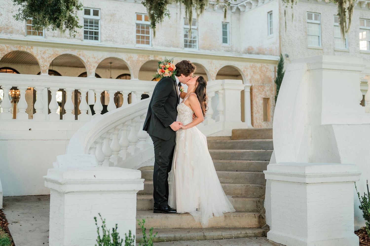 Elegant wedding couple embraces on grand marble staircase at luxurious estate venue.