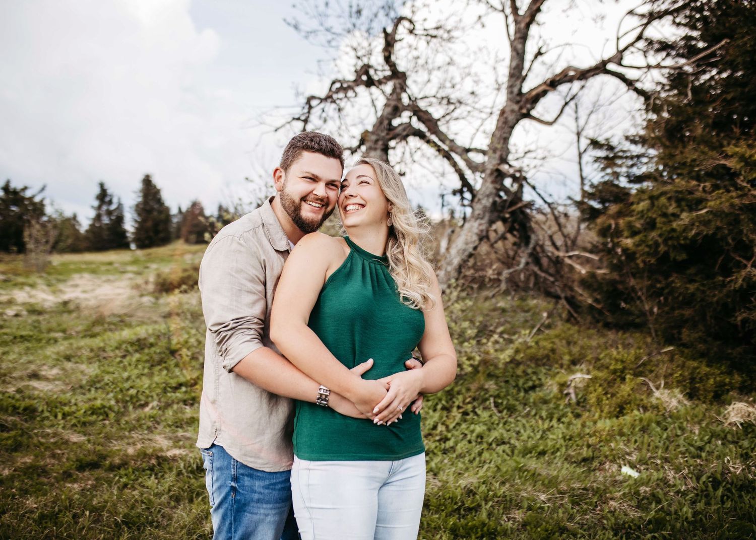 A couple in casual attire embraces and laughs together during an outdoor photoshoot in a natural setting.
