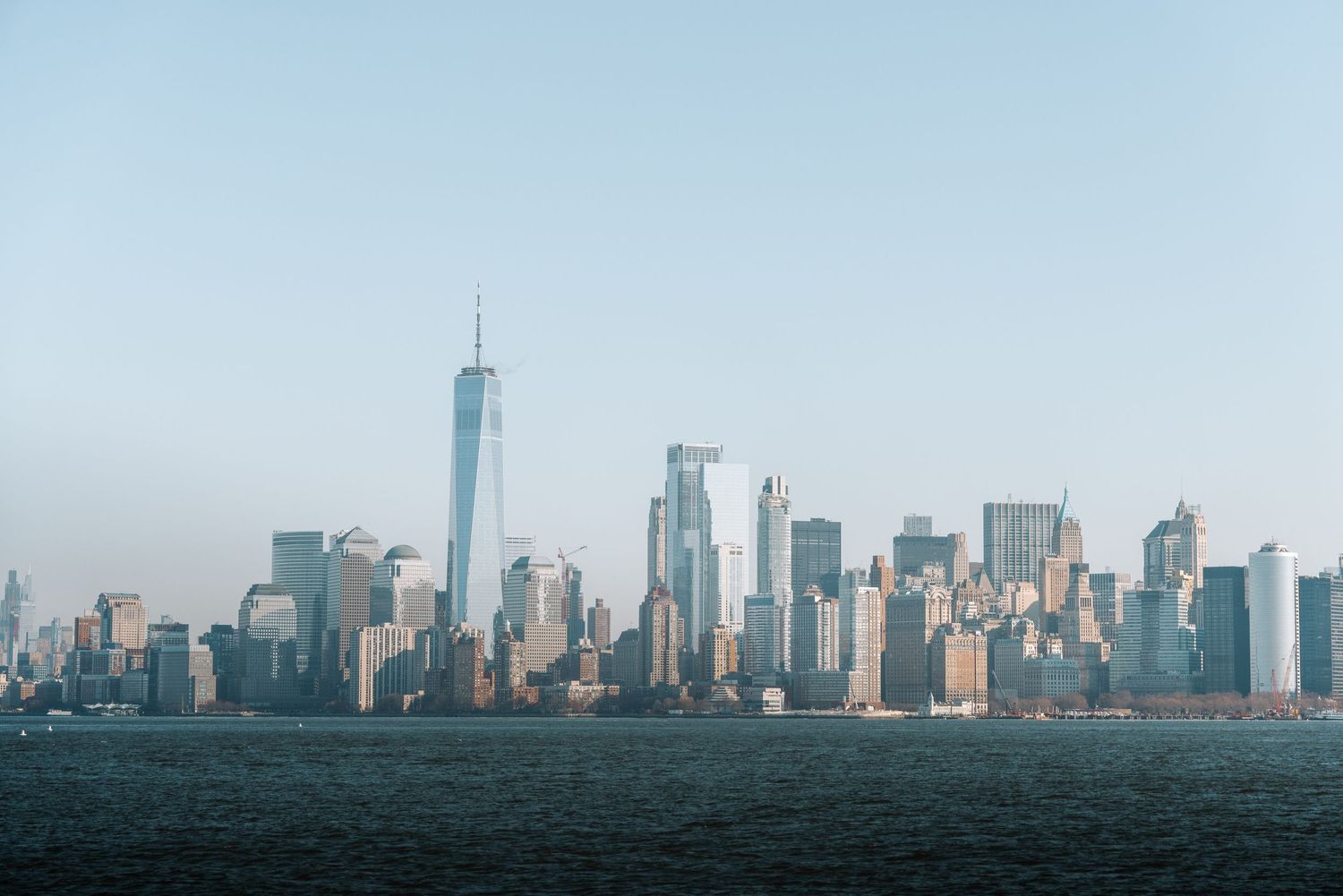 Panoramic skyline view of Manhattan with skyscrapers against hazy blue sky.