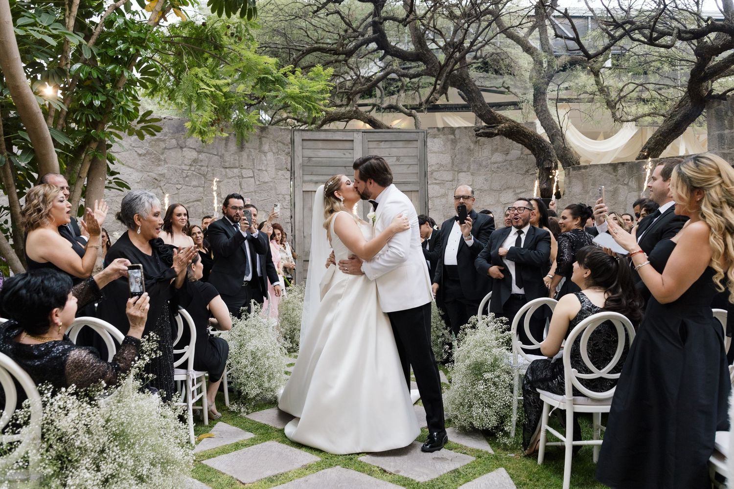 Wedding celebration in lush garden setting with guests watching the newlyweds.