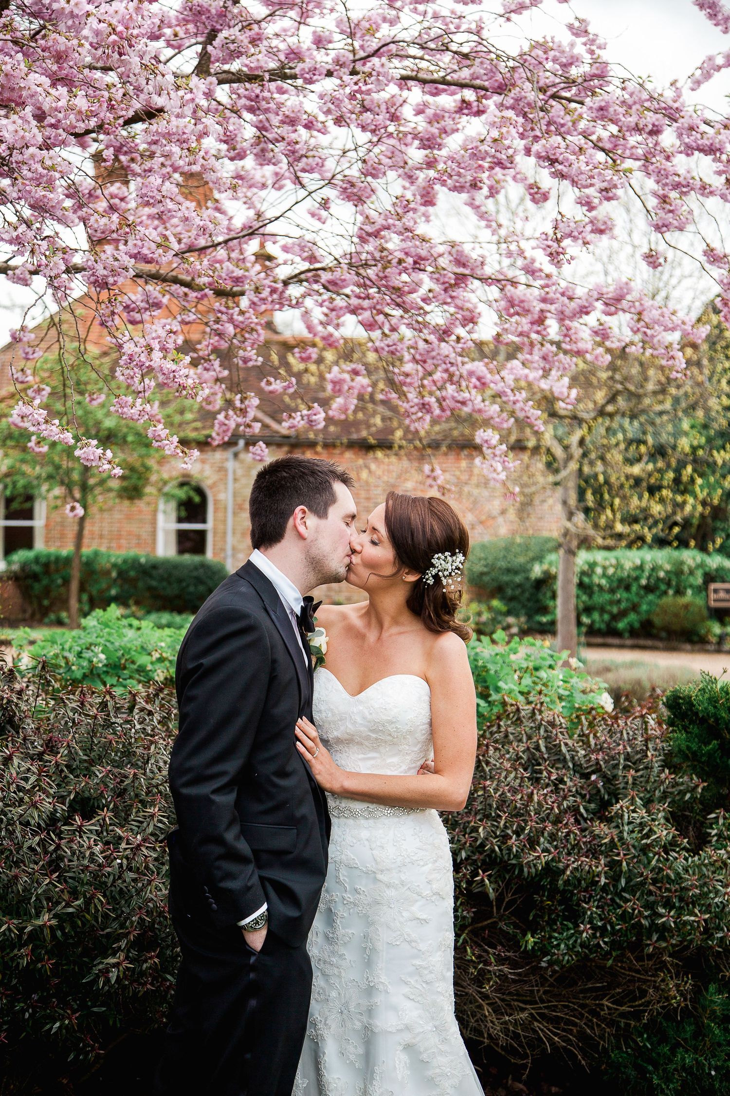 A couple walks through a scenic park with trees and a winding stream on their wedding day.