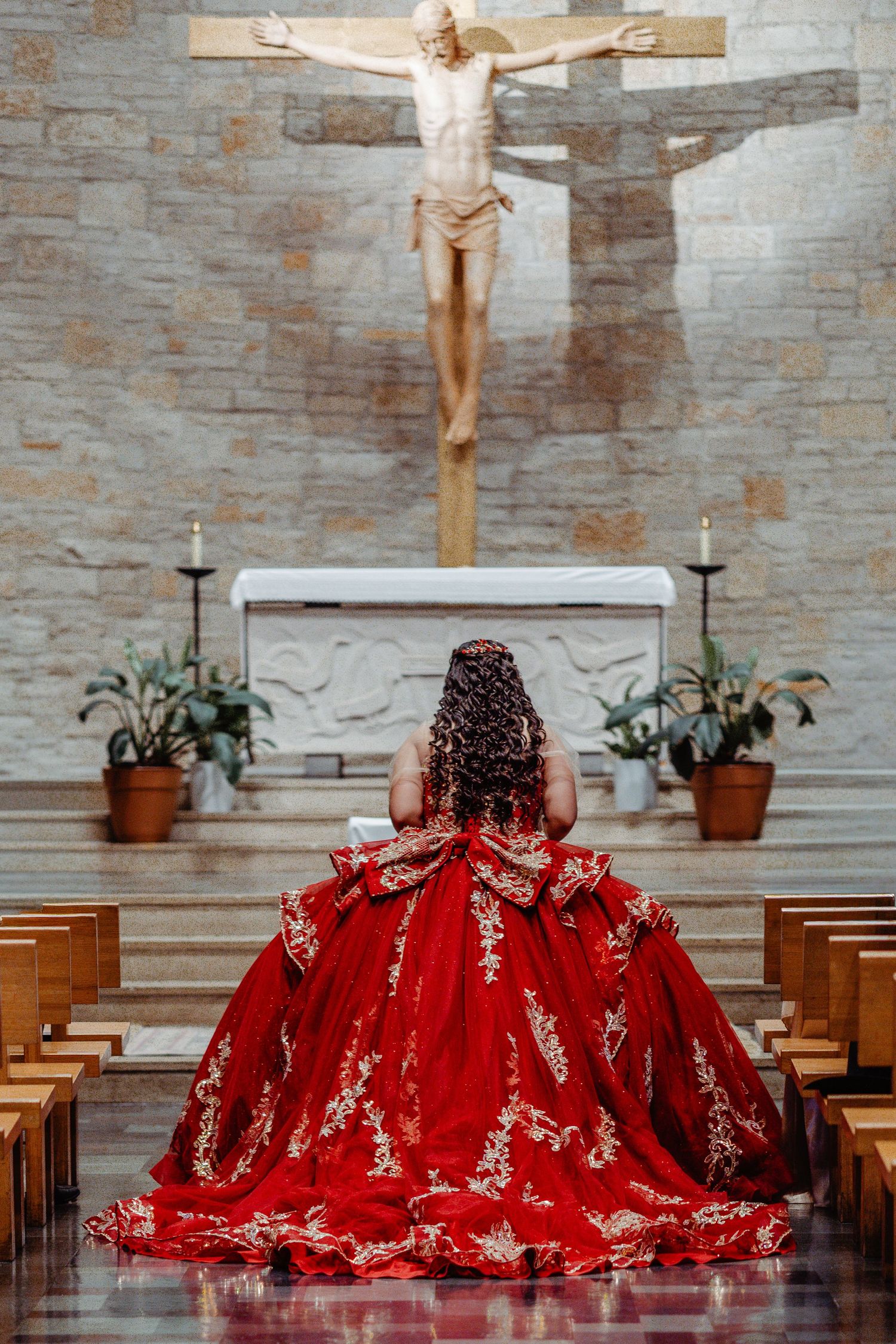 A dramatic red dress with lace details spreads across church pews beneath a crucifix in a stone chapel setting.
