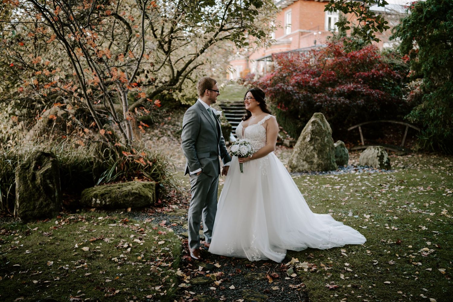 Wedding couple poses among lush greenery and white floral arrangements outdoors.