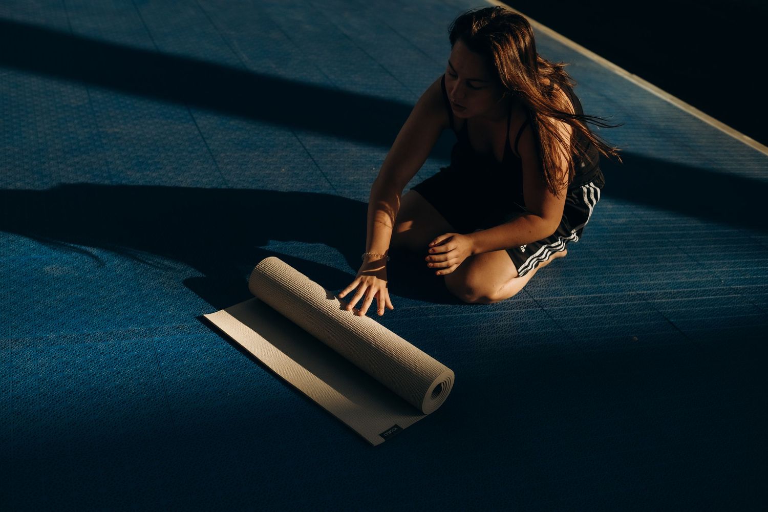 girl rolling a yoga mat in afternoon shadows after brand yoga event in Stockholm captured by Stockholm photographer for wellness brand event