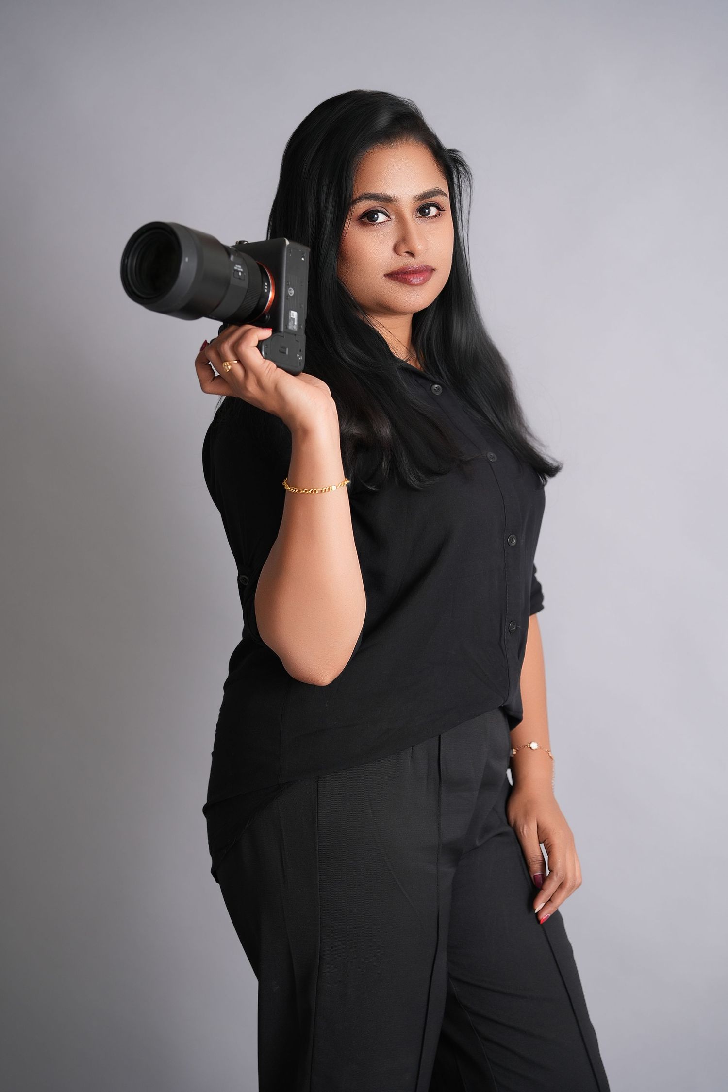 Professional photographer wearing all black poses with telephoto lens against gray studio backdrop in multiple angles.