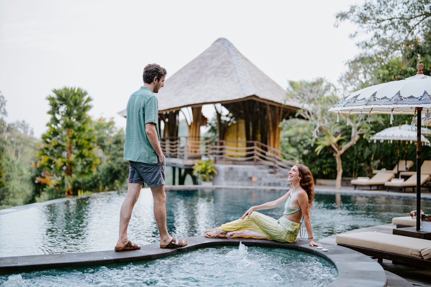 Couple walking along stone pathway through lush tropical garden setting.