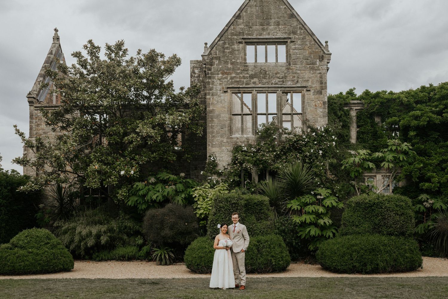 Bride and Groom standing together in front of historic ruins at Nymans Gardens on their wedding day in West Sussex
