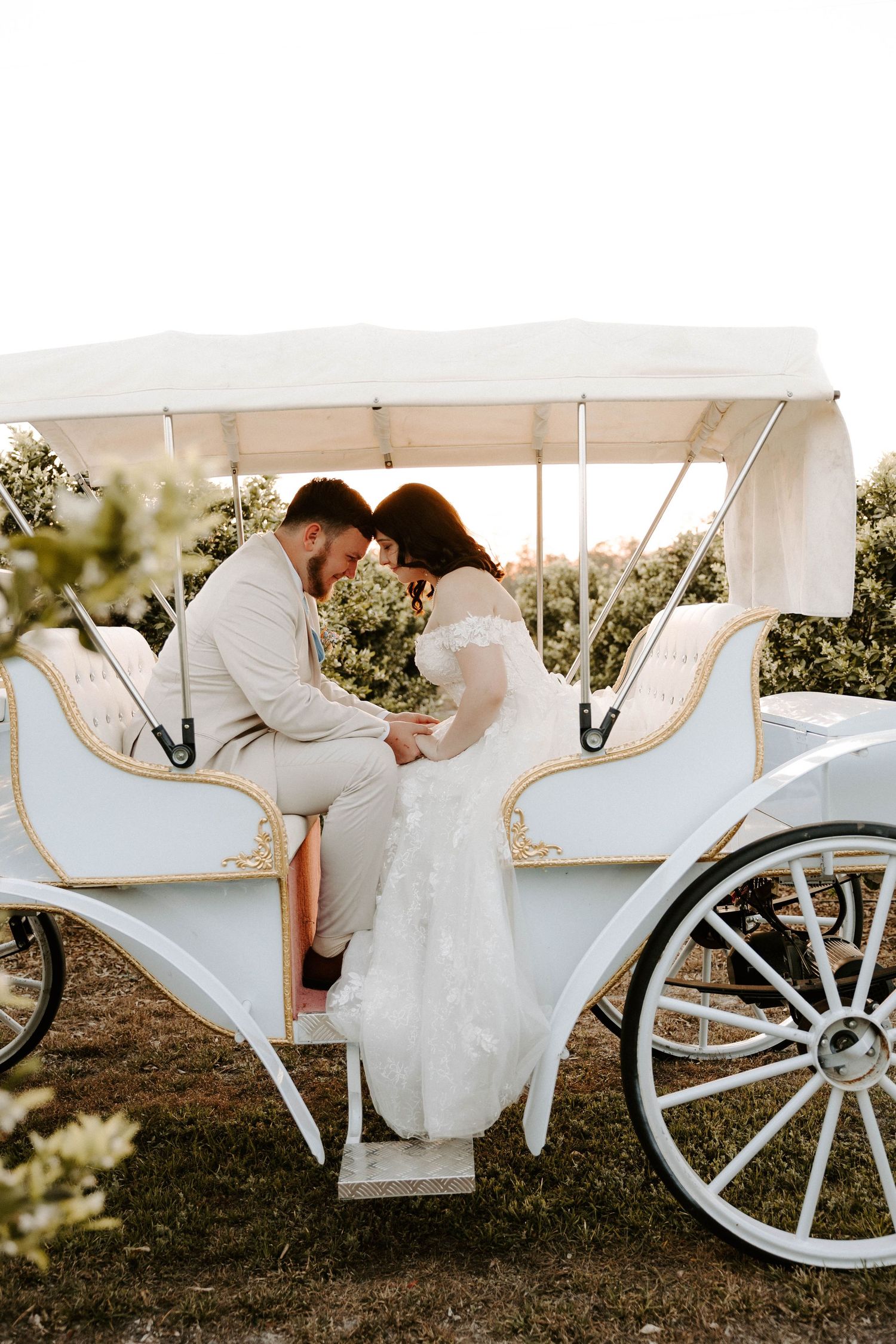 Newlyweds sharing romantic moment in elegant white carriage during wedding photoshoot.