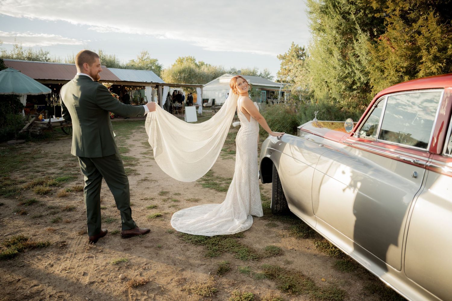 A classic champagne-colored vintage car is being photographed outdoors in a natural setting during a special occasion.