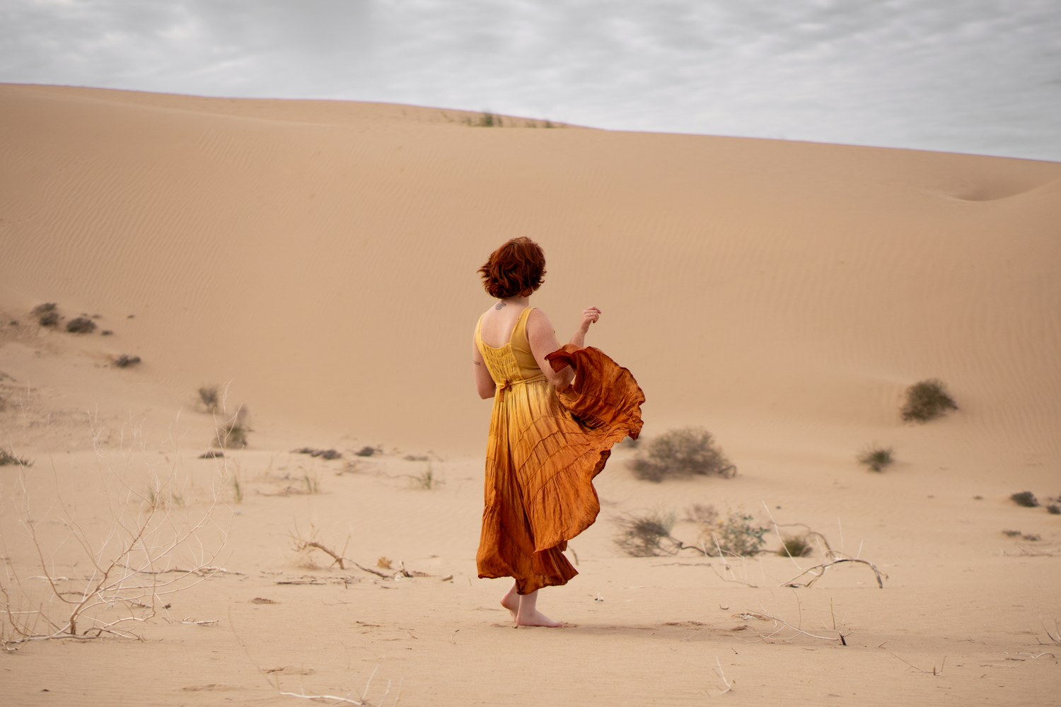woman poses in sand dunes wearing a brightly colored dress