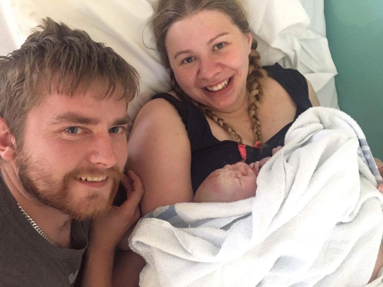 New parents resting on hospital bed with newborn baby.