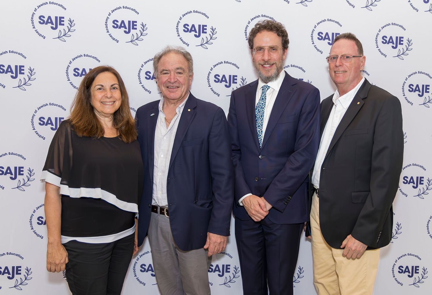 Professional group photo with four people posing in front of a branded backdrop with logos.