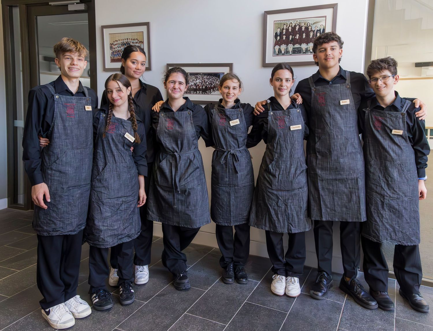 Seven staff members wearing matching dark denim aprons pose in a row.