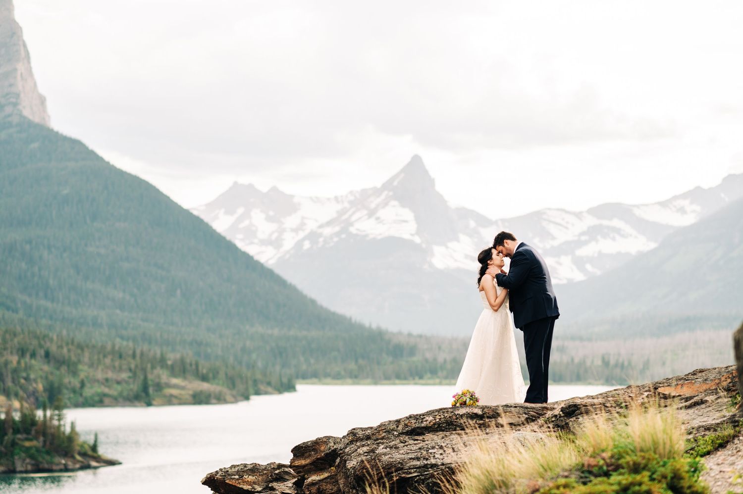 Couple in wedding attire in Glacier National Park, a lake and mountain are behind them in the image.
