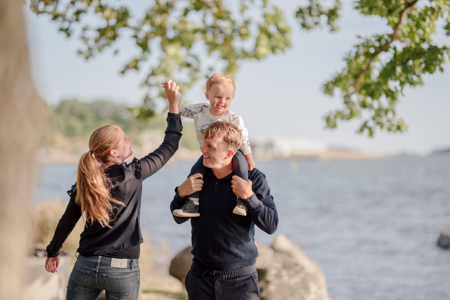 Family enjoying playful moment by waterfront under tree branches.