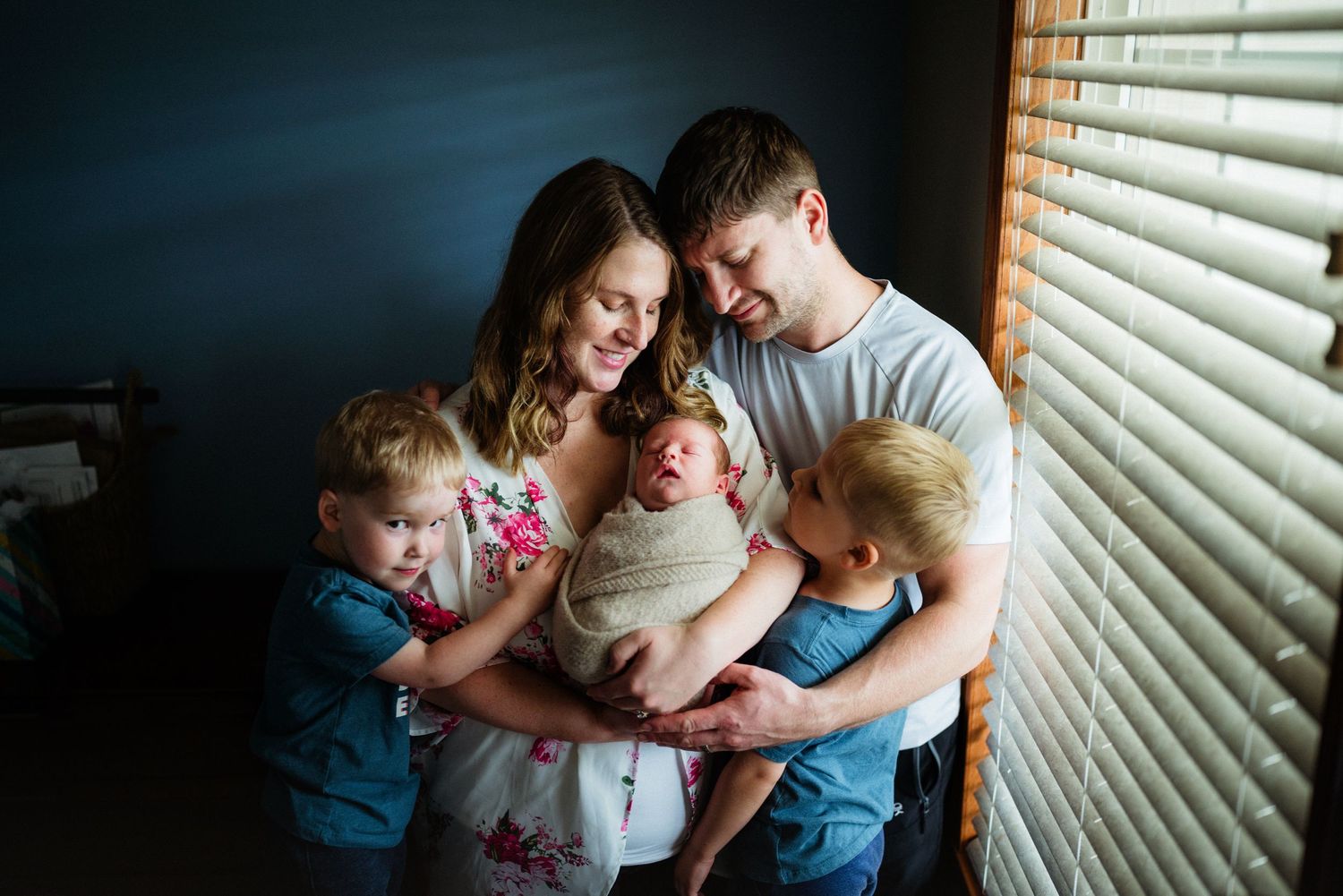 Family gathered by window sharing intimate moment with their newborn baby.