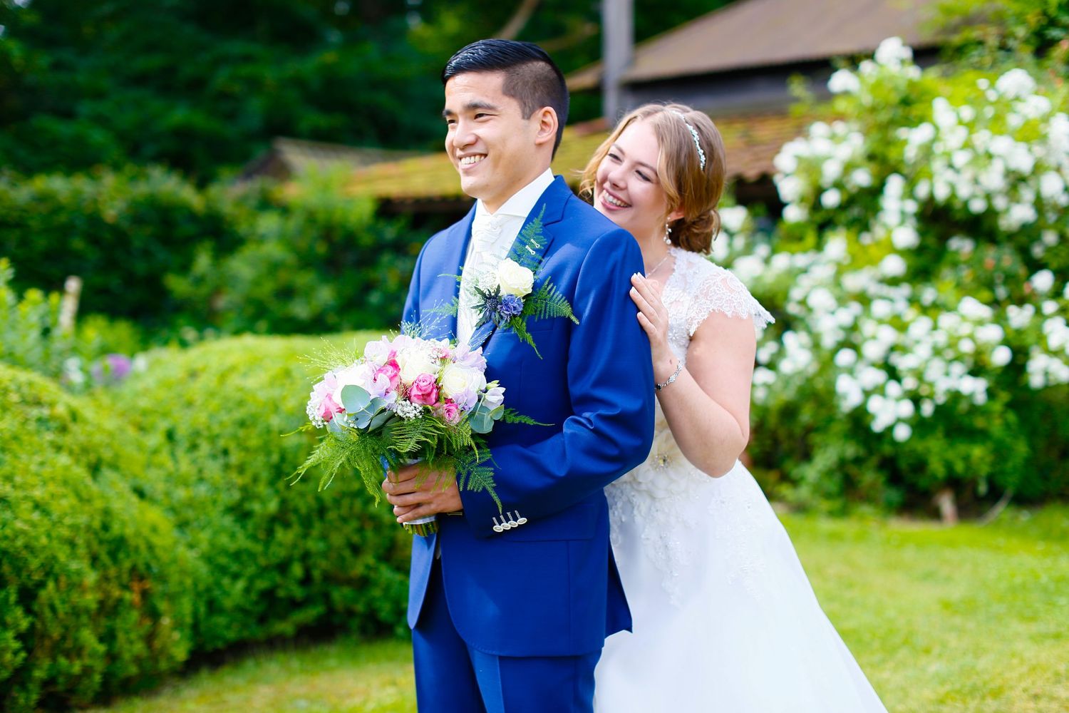 A couple poses with flowers in a garden setting on their wedding day.