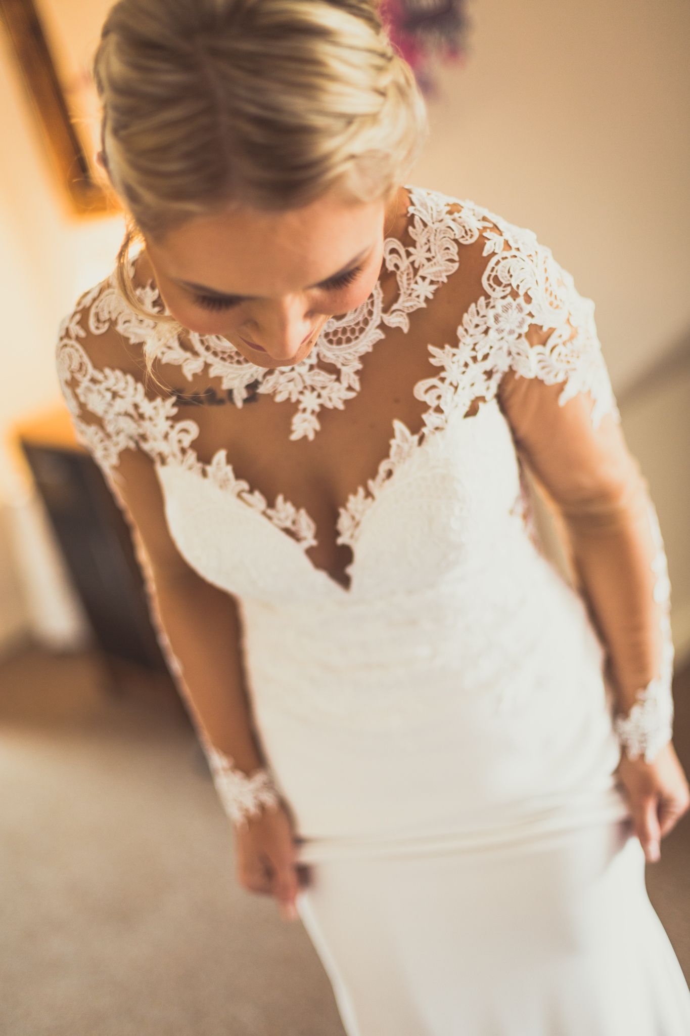 A wedding dress with intricate lace details and sheer neckline shown from above on a bride.