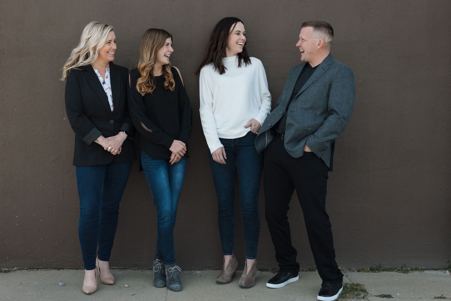 A group of four people wearing casual attire stand against a dark wall while engaged in conversation.
