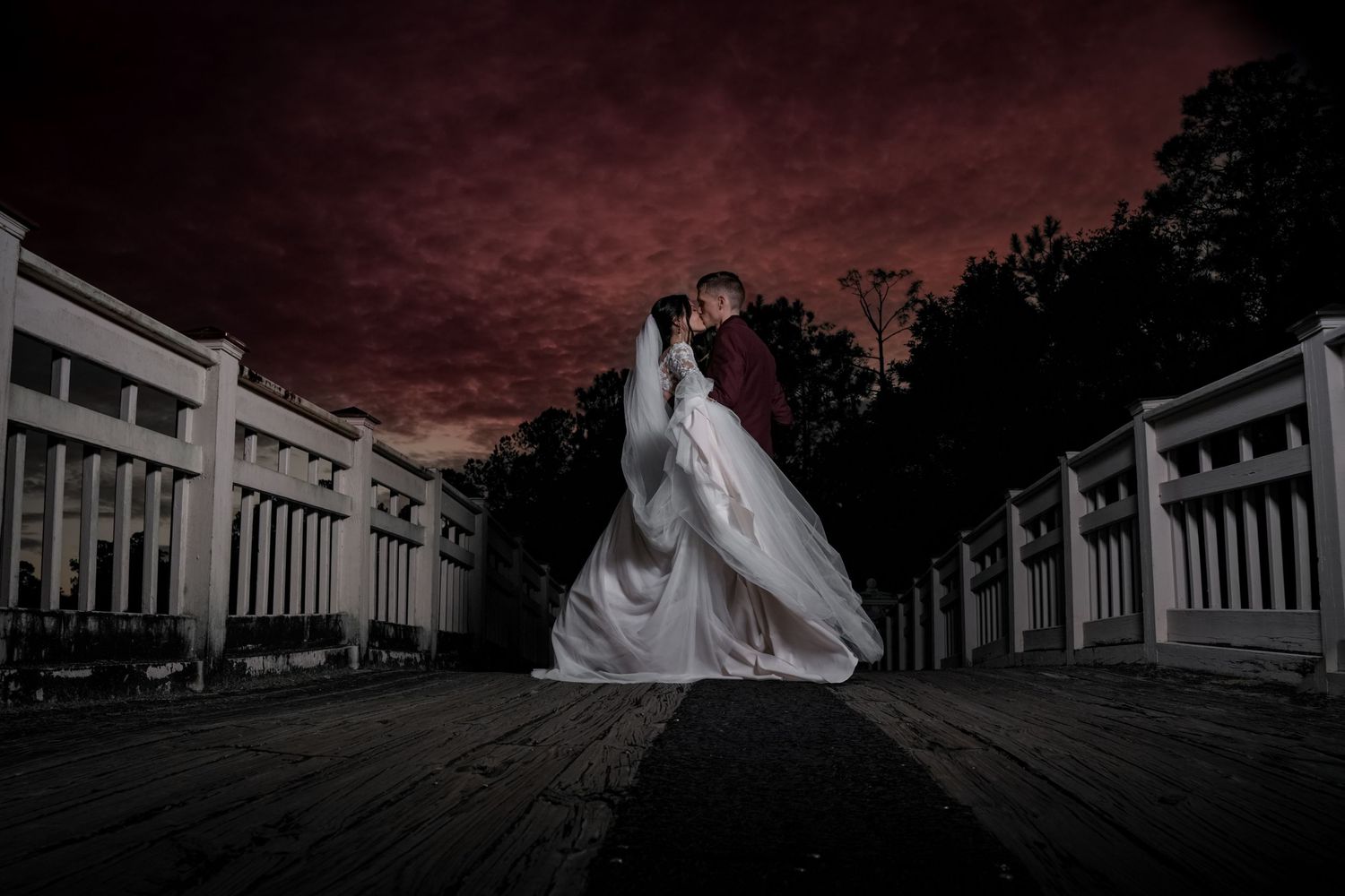 Dramatic wedding photo with couple silhouetted against dark red sky between columned walkway.