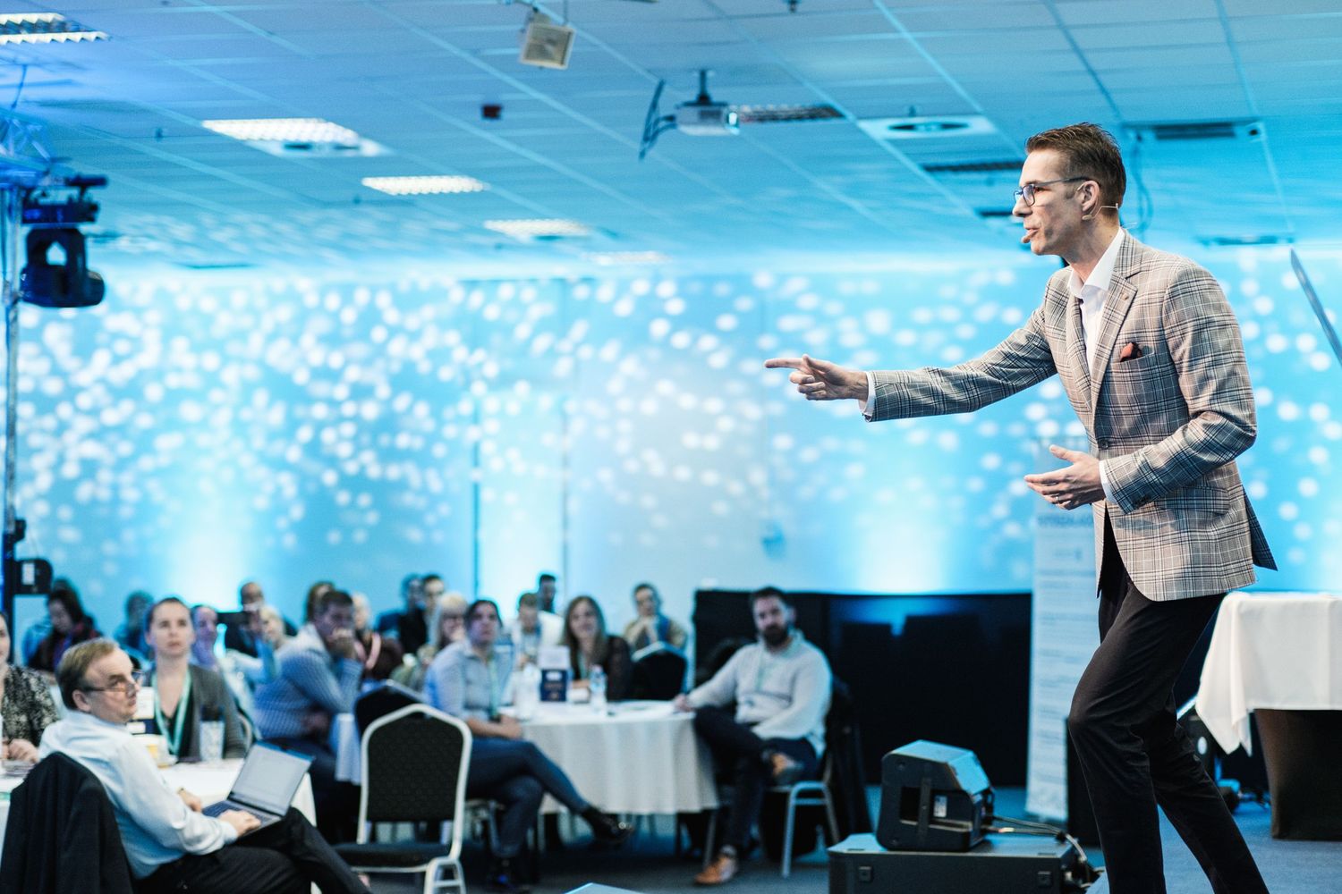 Speaker giving dynamic presentation in conference room with blue lighting effects.