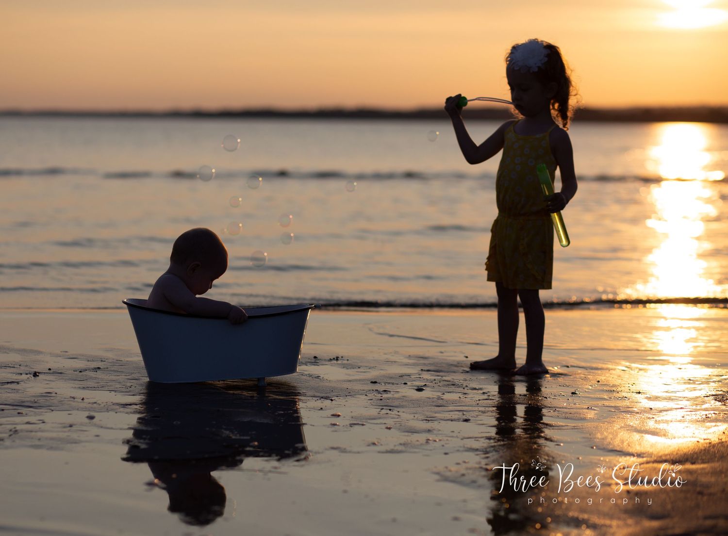 Silhouettes at sunset with a child standing by a tub on a beach.