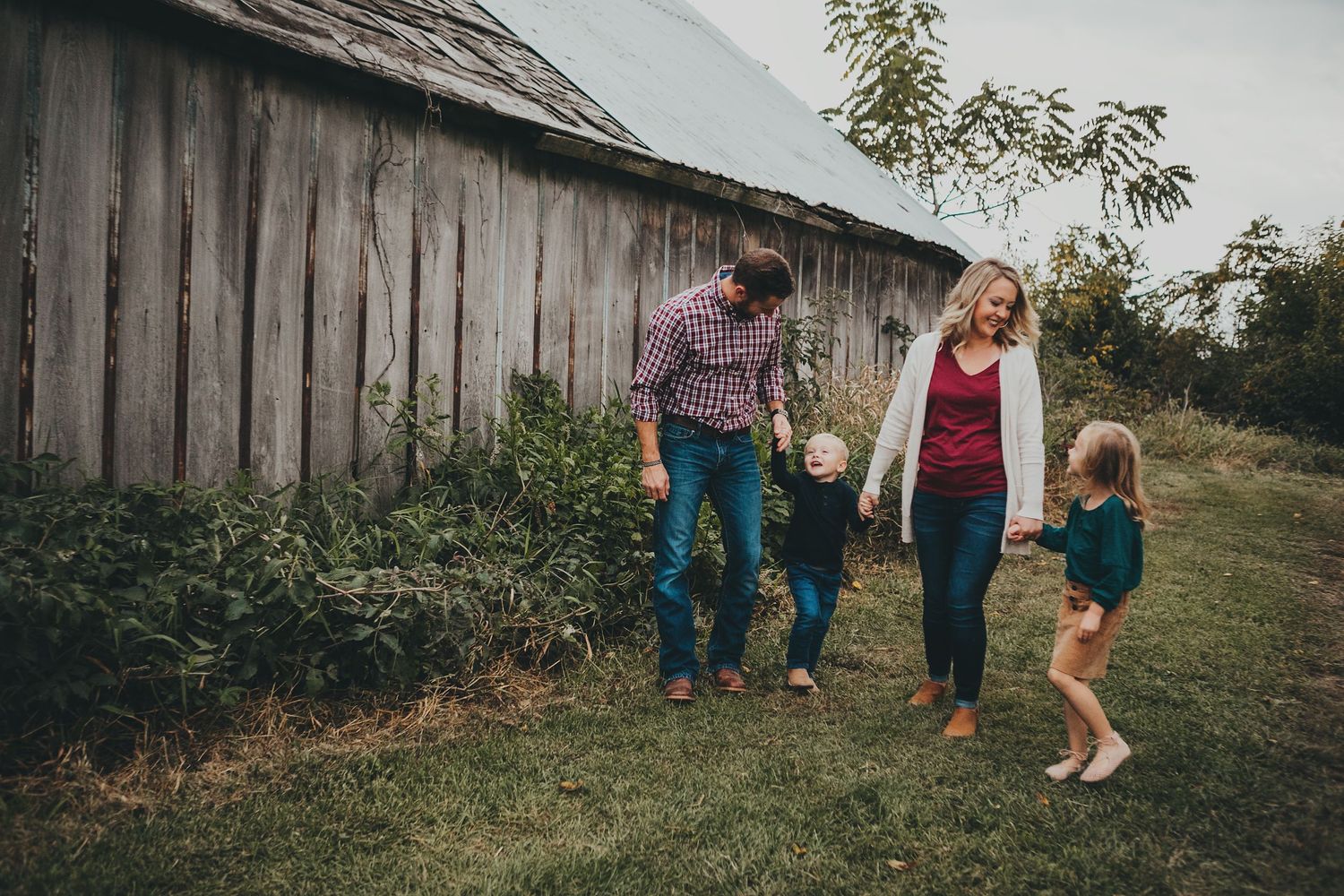 Family gathering outside rustic wooden barn in autumn setting.
