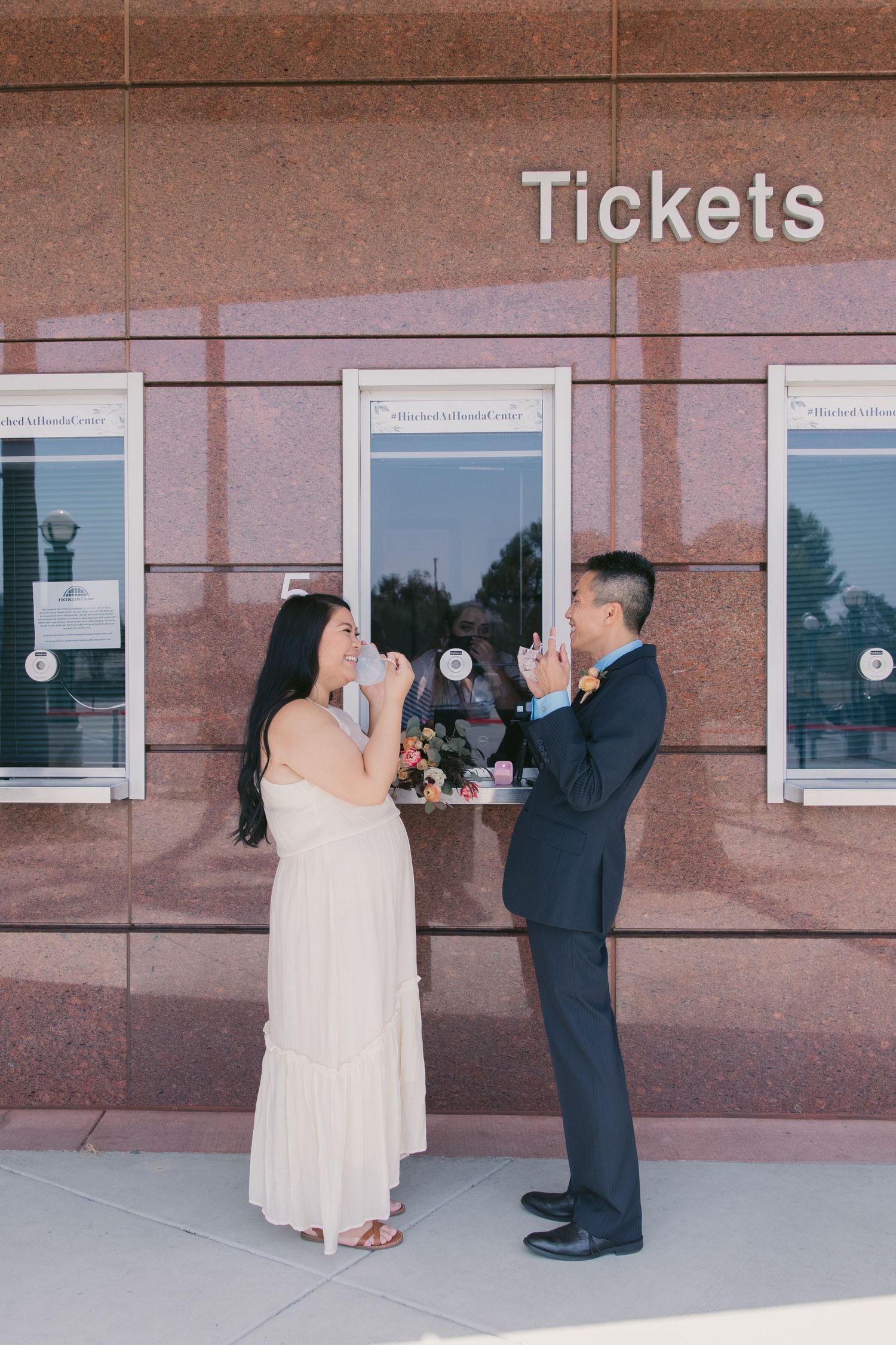 Wedding couple posing for photos near a ticket window at a venue.