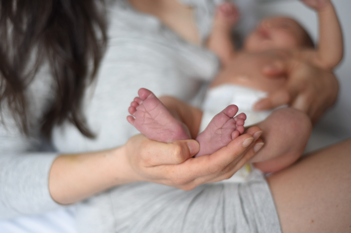 Close-up of tiny newborn baby feet cradled in gentle hands.