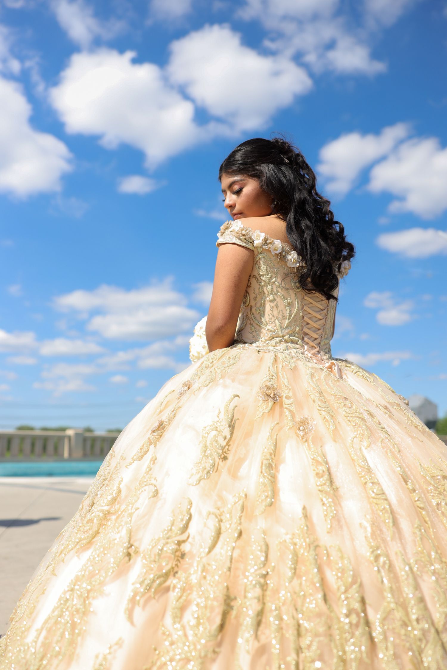 A beautiful champagne-colored ball gown with detailed embroidery captured against a bright blue sky.