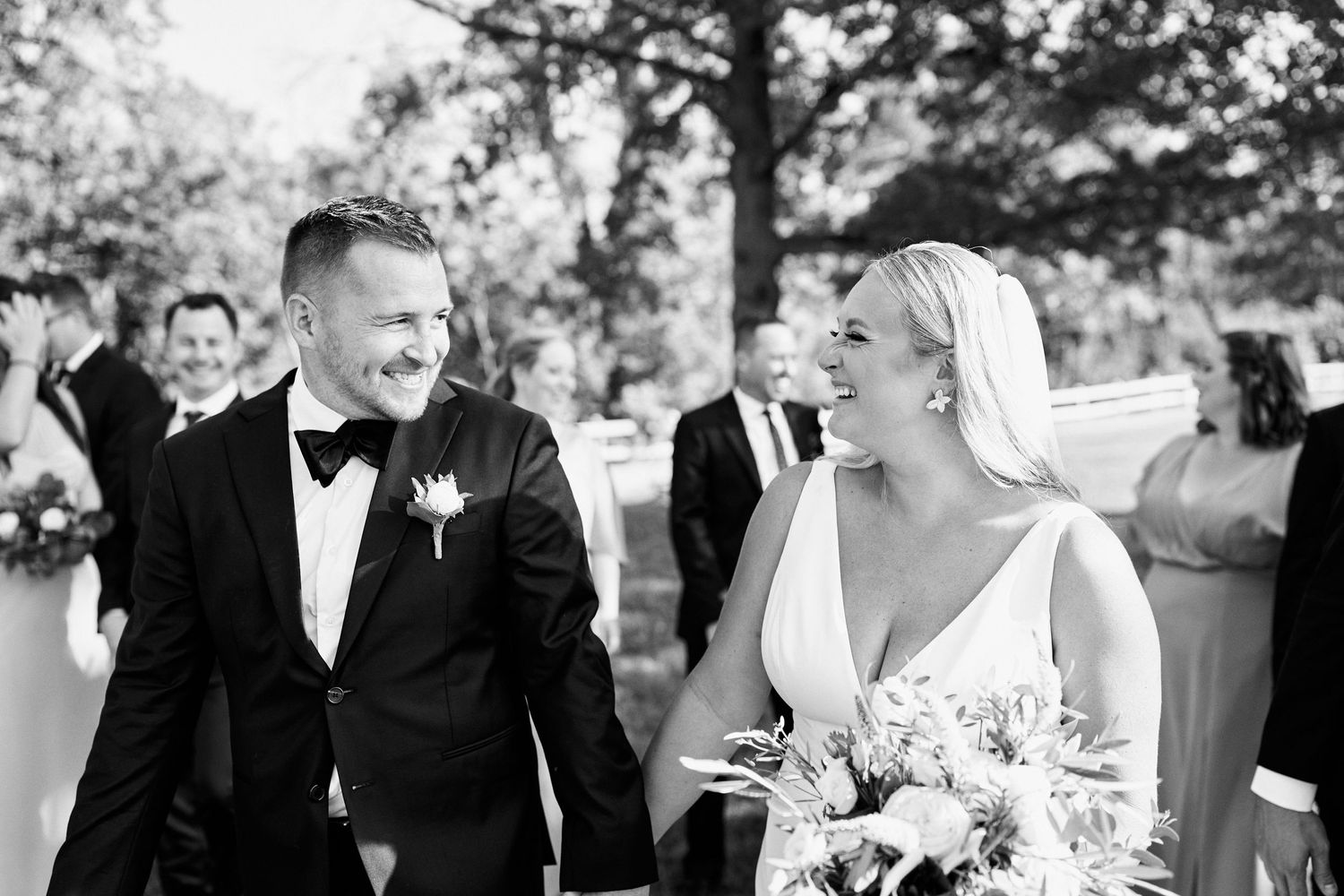 A candid black and white wedding photo showing laughter during an outdoor ceremony.