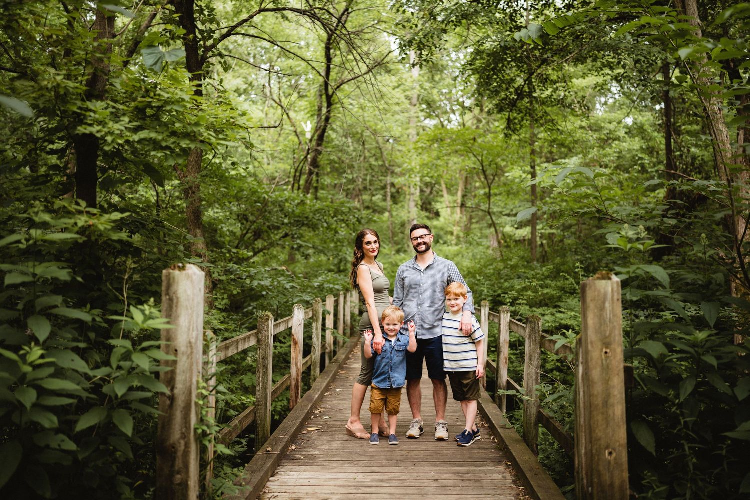 Family portrait on wooden bridge surrounded by dense forest foliage.