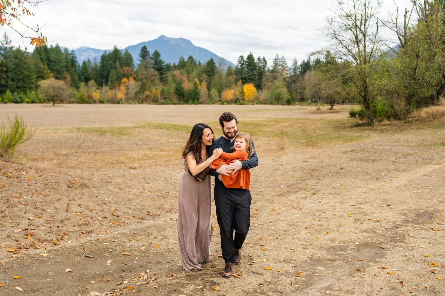 Family cuddling with their daughter with a backdrop of fall leaves and mountains in North Bend.