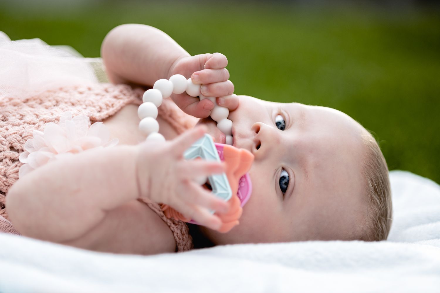 Adorable baby lying on white blanket wearing pink outfit and playing with their feet.