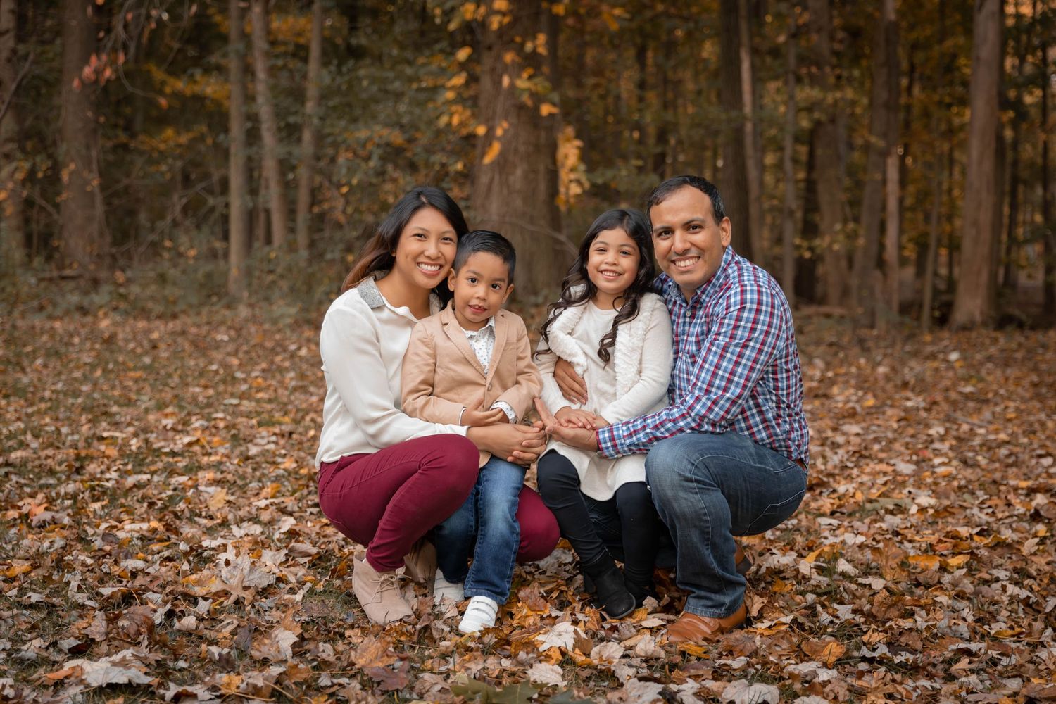 Family of four sitting together on autumn leaves in a wooded forest setting.