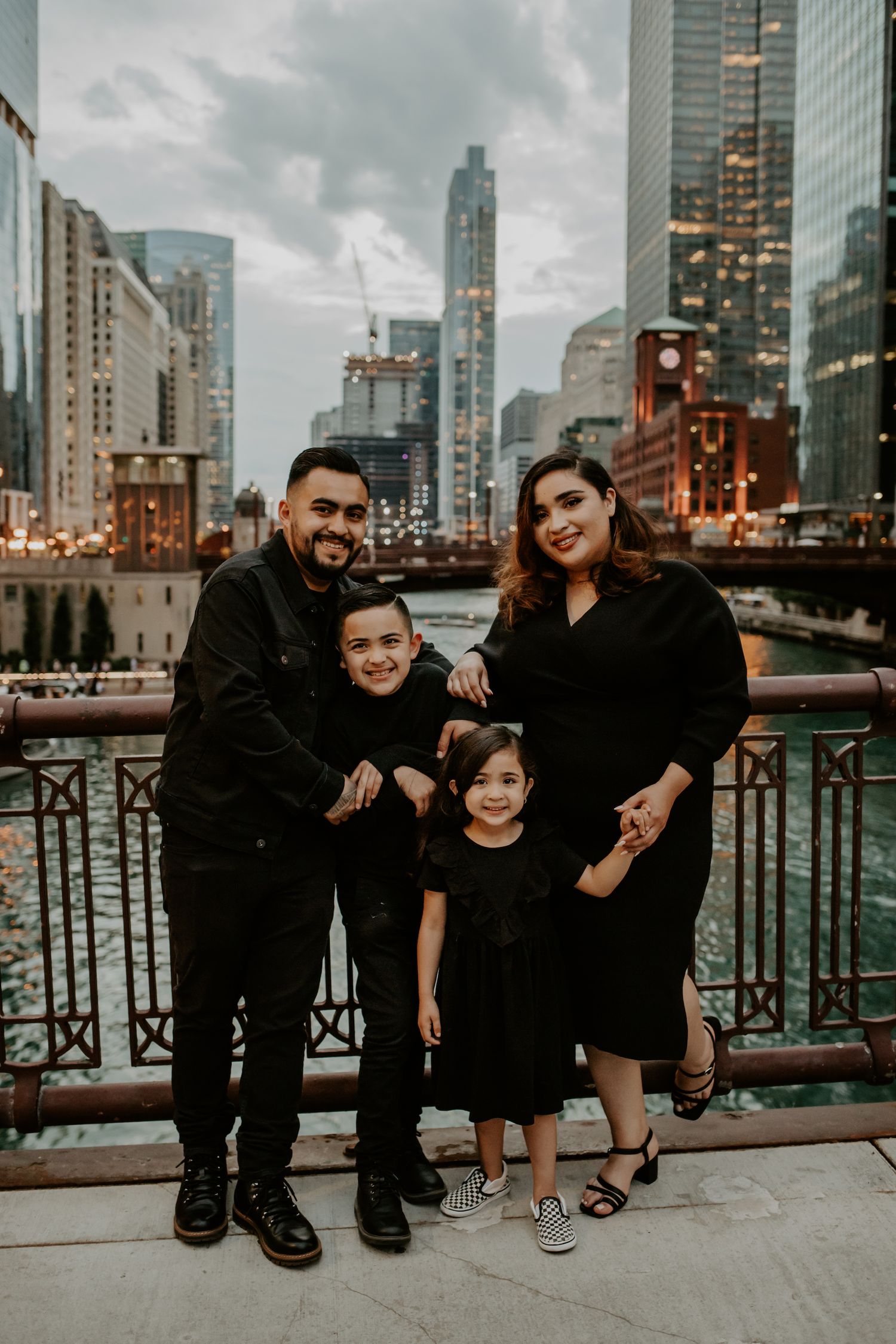 A family poses together on a bridge with Chicago's skyline and river in the background at dusk.