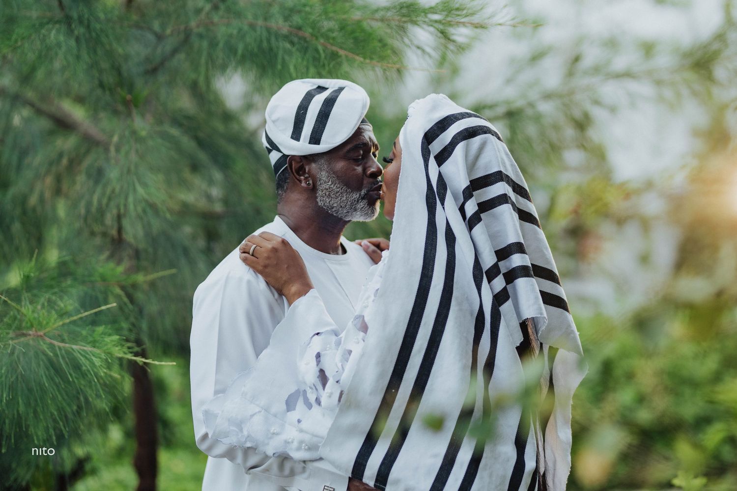 A person wearing white garments holds striped fabric against a green natural background.