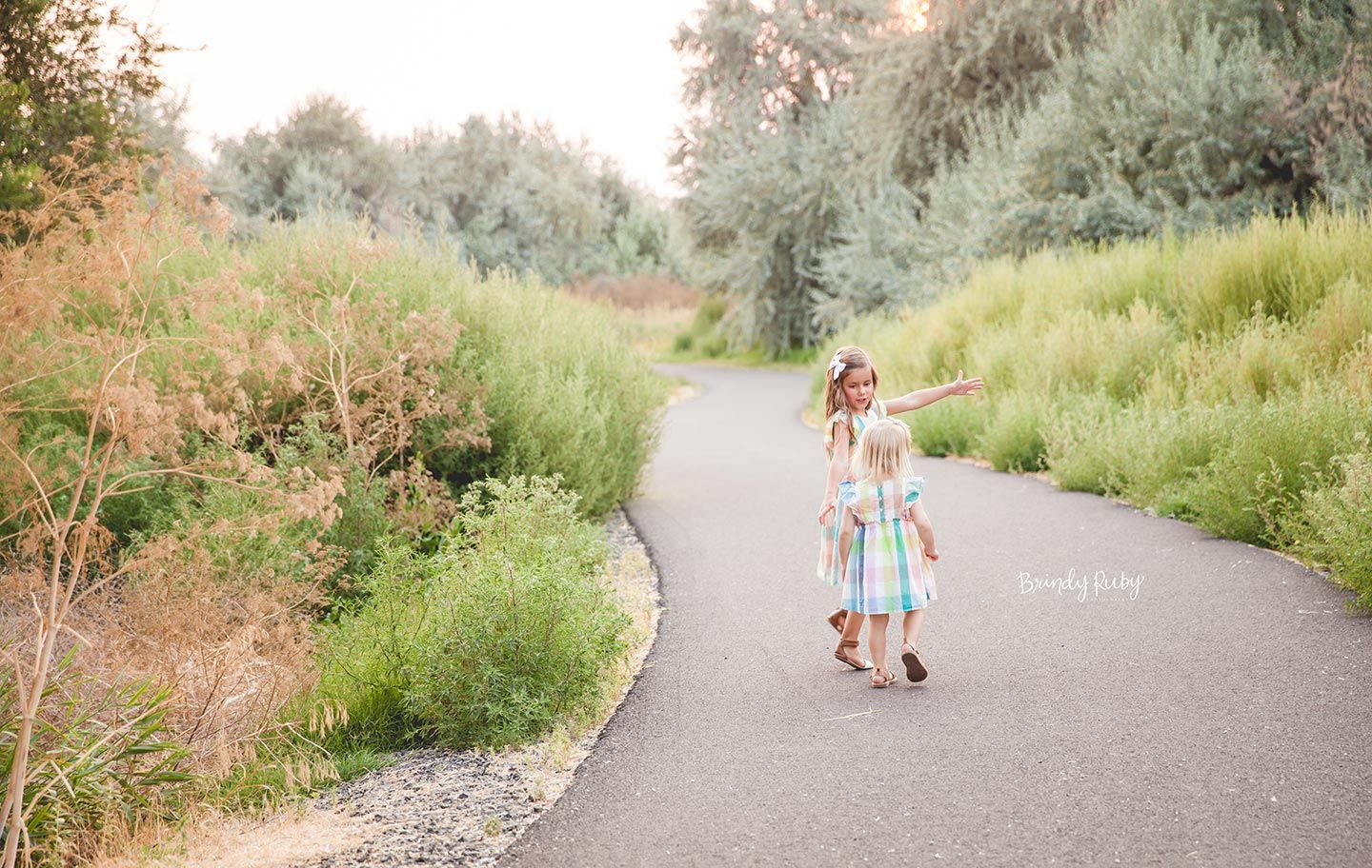 sisters walking down trail between tall weeds, playing and dancing together in Easter dresses