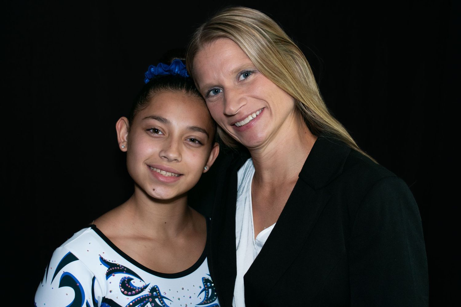 Two people pose together against a black background wearing blue and white outfits.